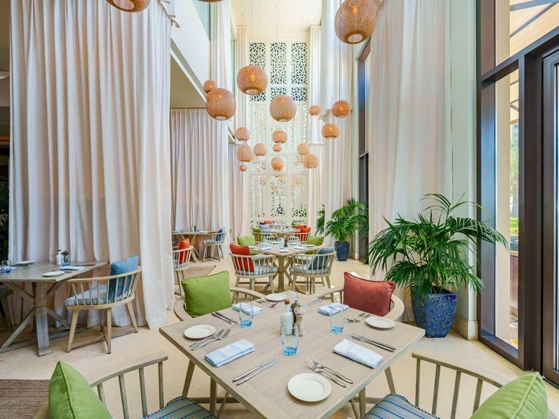 Ein heller Hotelgastraum mit hohen Decken, hängenden Lampen und bunten Sesseln.