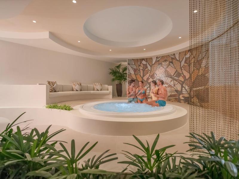 Modernes Spa mit rundem Whirlpool, gemütlichen Sitzecken und Pflanzen in warmem Ambiente.