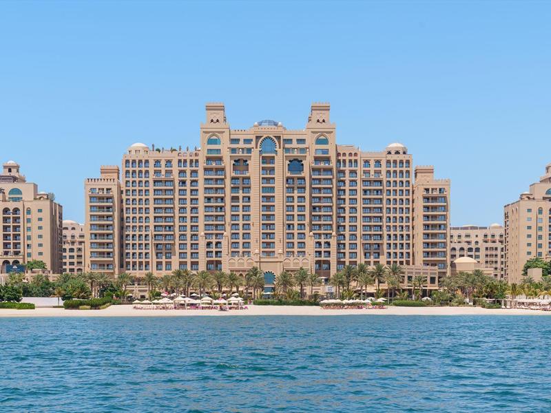 Großes, sandfarbenes Hotel am Meer mit vielen Balkonen und blauem Himmel im Hintergrund.