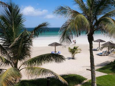 Strand mit Palmen, Liegestühlen und Sonnenschirmen bei klarem Himmel und blauem Meer