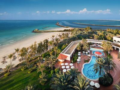 Hotel mit Pool und Zugang zum Strand an einer Küste mit klarem Himmel und ruhigem Meer.