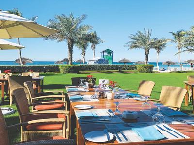 Restaurantterrasse mit gedeckten Tischen und Blick auf Meer und Palmen bei klarem Himmel.