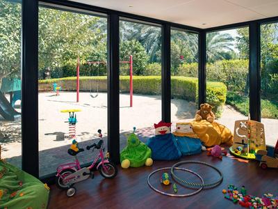 Kinder-Spielzimmer mit breiten Fenstern und Blick auf einen Sandkasten mit Schaukeln