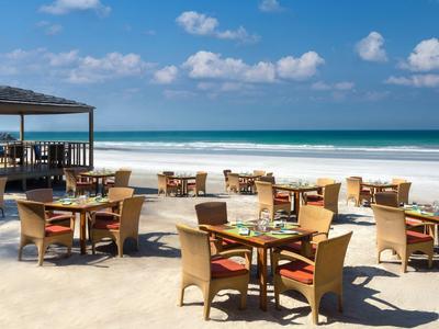 Strandrestaurant mit Tischen und Stühlen auf Sand mit Blick auf das Meer und blauen Himmel.