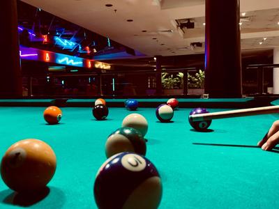 Nahaufnahme eines Billardtisches mit bunten Kugeln und einem Spieler, der eine Kugel stößt.