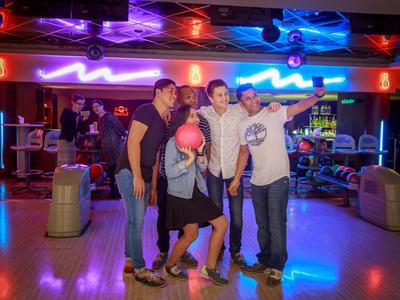 Gruppe von vier Personen posiert mit Bowlingkugel in einer Bowlingbahn.