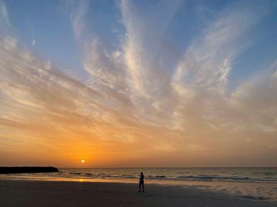 Sonnenuntergang über ruhigem Meer mit einer einzelnen Person am Strand.