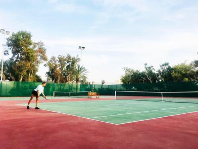 Eine Person spielt Tennis auf einem Außenplatz mit rotem und grünem Belag.