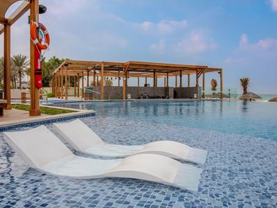 Ein Pool mit eingebauten Liegen und einer Holz-Pergola im Hintergrund bei sonnigem Wetter.