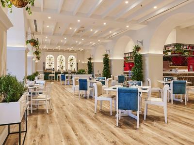 Helles, modernes Restaurant mit weißen Möbeln, blauen Stühlen und Holzfußboden in einem Hotel.