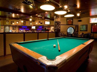 Dunkler Raum mit großem Billardtisch in der Mitte und gemütlicher Beleuchtung.