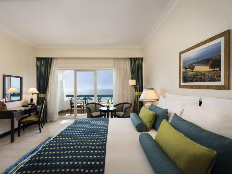 Helles Hotelzimmer mit Doppelbett, Sitzbereich und Balkon mit Meerblick.