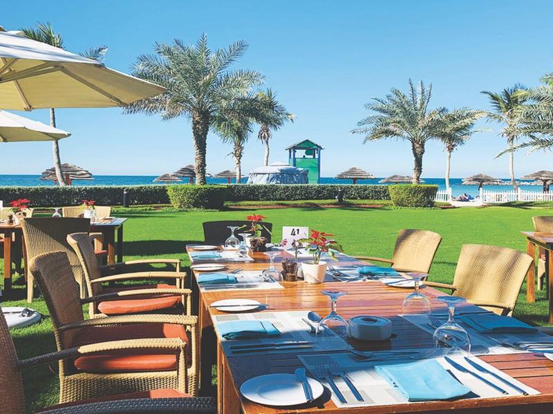 Restaurantterrasse mit Tisch und Stühlen im Freien, Blick auf Palmen und Meer