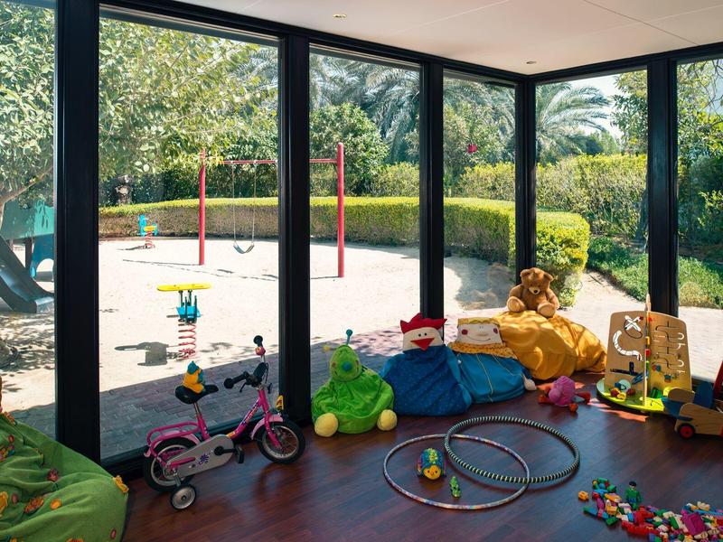 Kinder-Spielzimmer mit breiten Fenstern und Blick auf einen Sandkasten mit Schaukeln