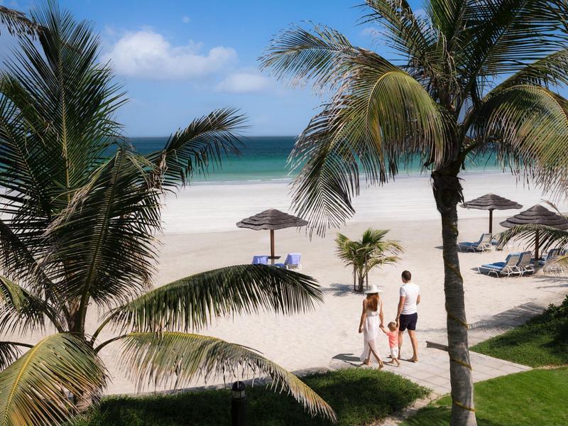 Tropischer Strand mit Palmen, weißen Sand und Paar, das am Wasser entlanggeht.