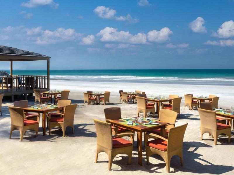 Strandrestaurant mit Strohschirm und leeren Stühlen an einem sonnigen Tag.