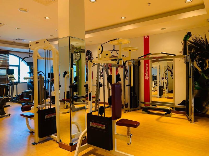 Moderner Fitnessraum im Hotel mit Trainingsgeräten und Hanteln auf hellem Holzboden.