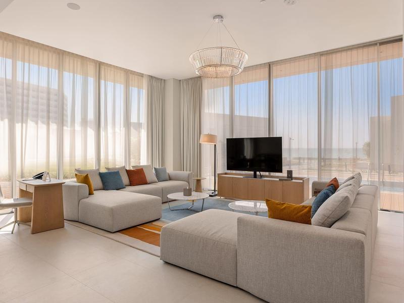 Helles Wohnzimmer mit großen Fenstern, grauem Ecksofa, Holztisch und modernem Fernseher.