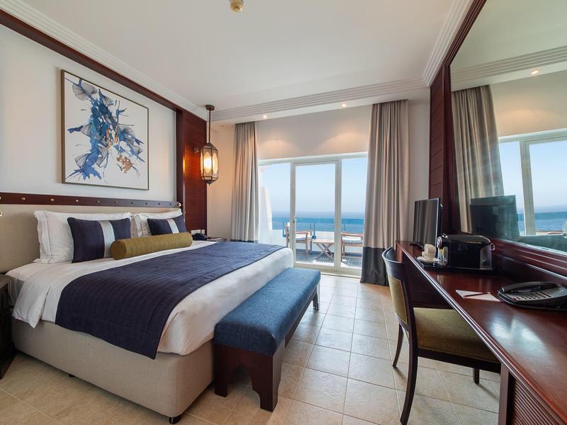 Modernes Hotelzimmer mit Doppelbett, Schreibtisch und Meerblick durch große Fenster.