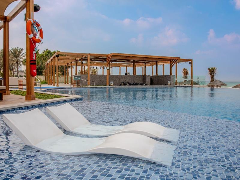 Infinity-Pool mit eingebauten Liegen und Holzpavillon unter blauem Himmel