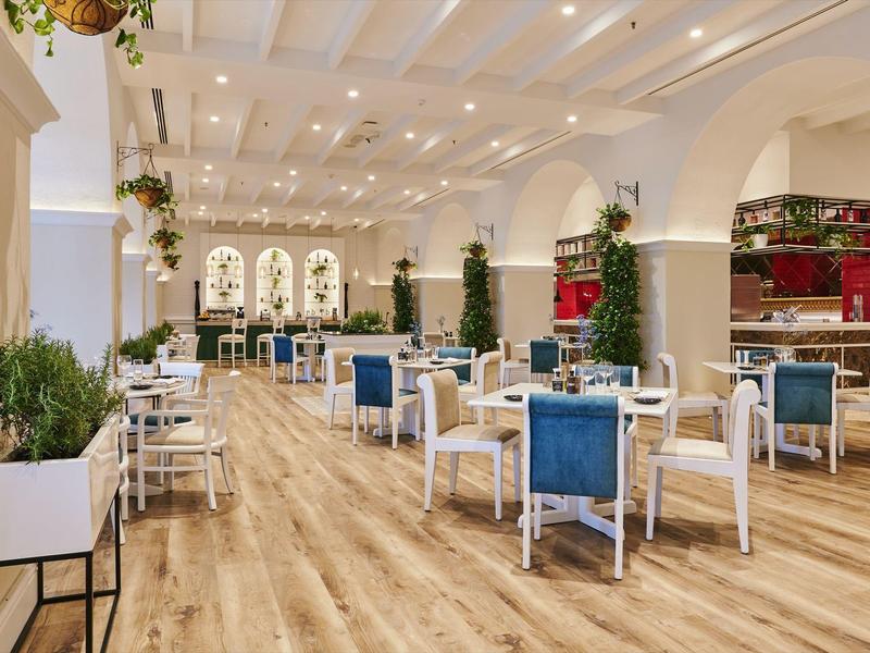 Heller, moderner Speisesaal mit Holzfußboden, blauen Stühlen und großen Fenstern.