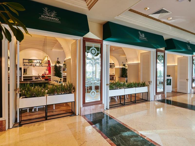 Eleganter Eingangsbereich eines luxuriösen Hotels mit grünen Markisen und dekorativen Pflanzen.