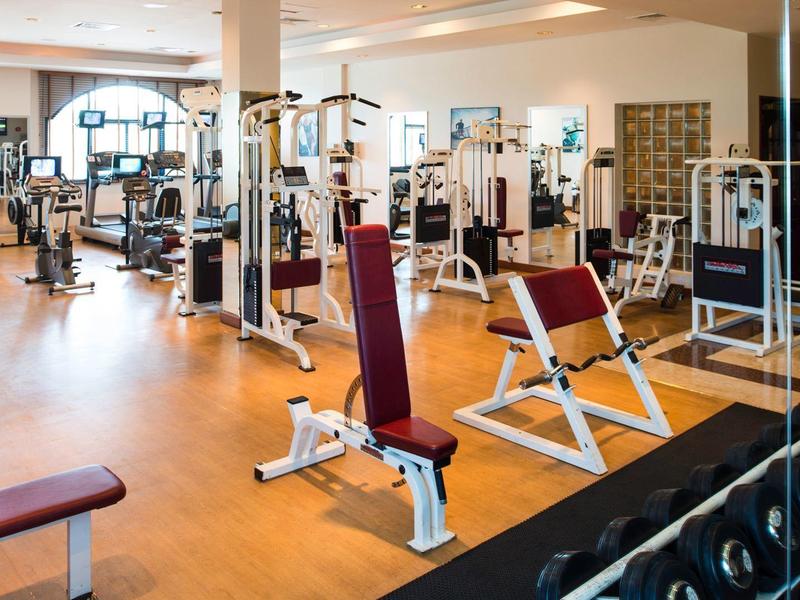 Großer Fitnessraum mit verschiedenen Trainingsgeräten und Freihanteln auf Holzfußboden.