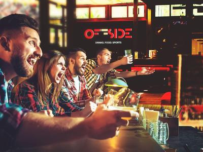 Skupina přátel, kteří se smějí a pijí společně v baru v živé atmosféře.