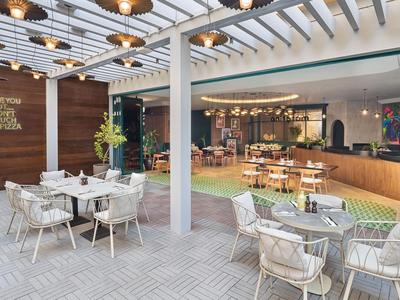 Moderner Hotelrestaurantbereich mit hellen Tischen, Stühlen und dekorativer Beleuchtung unter Pergola.