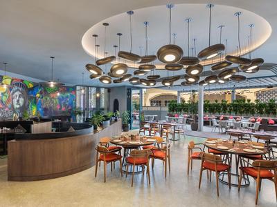 Modernes Hotelrestaurant mit runden Holztischen, orangen Stühlen und einem großen Deckenvorhang.