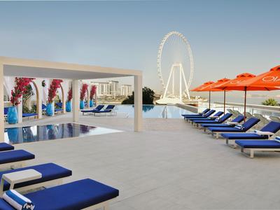 Moderner Poolbereich mit blauen Liegestühlen, orangefarbenen Sonnenschirmen und großem Riesenrad im Hintergrund.