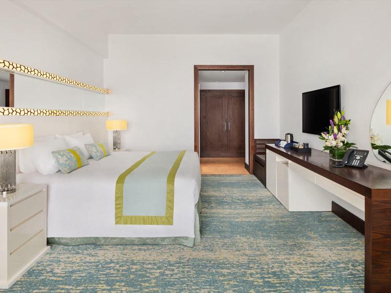 Chambre d'hôtel lumineuse avec grand lit, bureau et télévision murale.