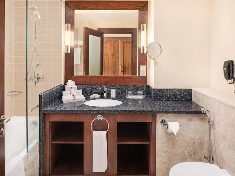 Salle de bain simple avec meuble en bois, plan de travail en granit et miroir éclairé.