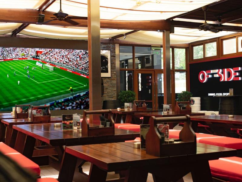 Bar sportif confortable avec mobilier en bois, match de football éclairé sur grand écran.