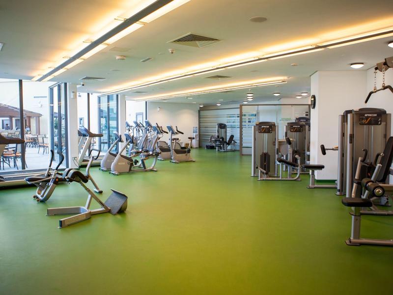 Grande salle de sport avec divers appareils d'entraînement et sol vert.