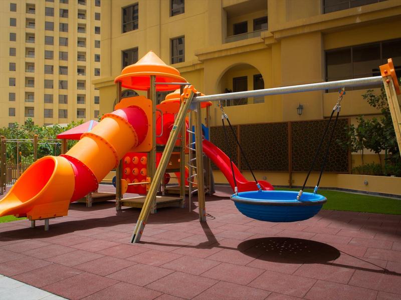 Aire de jeux colorée pour enfants avec toboggan, balançoire et structures d'escalade devant un immeuble.