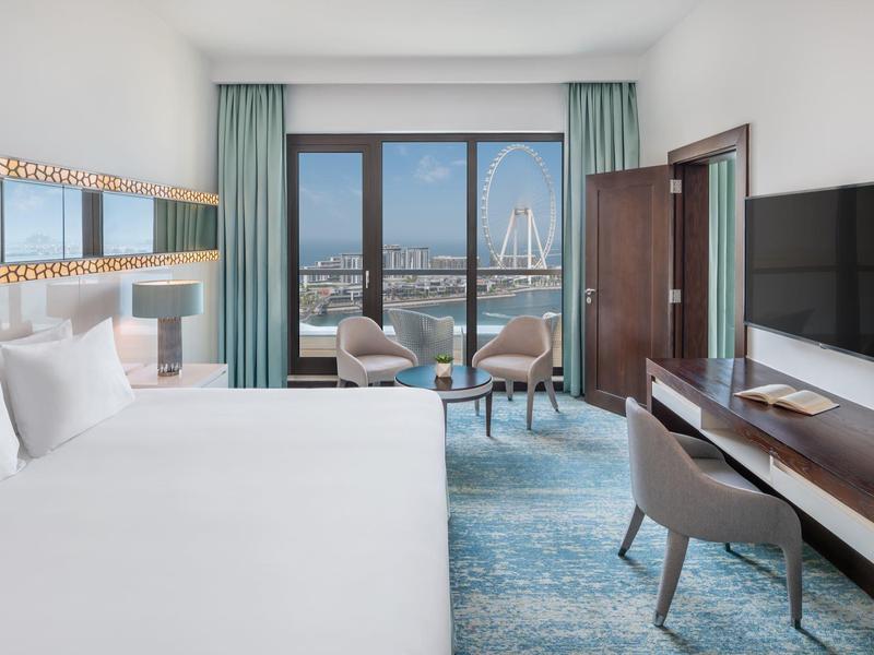 Chambre d'hôtel moderne avec grand lit, bureau et balcon avec vue sur la ville.