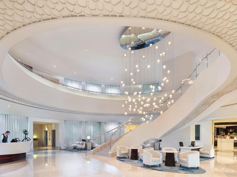 Hall d'hôtel lumineux et moderne avec escalier courbé et coin salon accueillant.