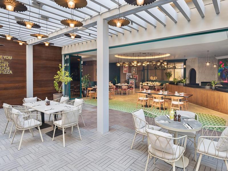 Espace extérieur moderne d'un hôtel avec tables, chaises et éclairage décoratif.