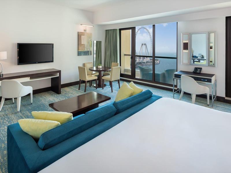 Chambre d'hôtel moderne avec vue sur la mer, bureau et coin salon confortable avec canapé.