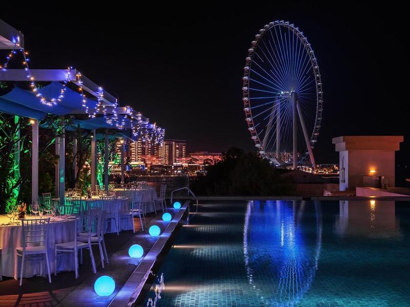 Espace piscine nocturne avec grande roue illuminée et salon confortable