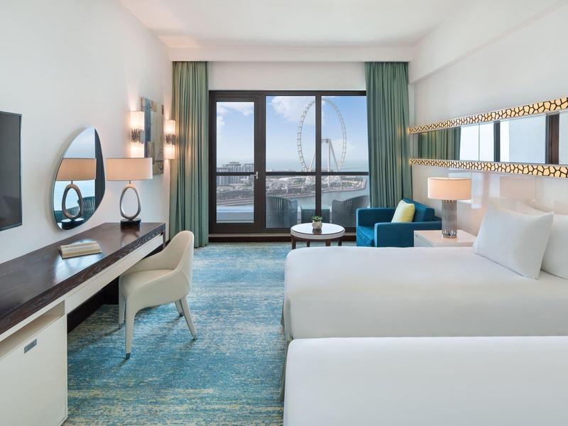 Chambre d'hôtel moderne avec deux lits, bureau et grande fenêtre avec vue.