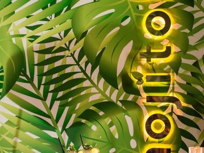 Grüner Blattmuster-Hintergrund mit goldfarbenem "mojitobar"-Schriftzug und Kerzen auf Holztisch.