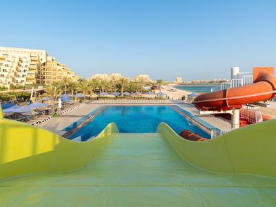 Wasserpark mit gelber Wasserrutsche, blauem Pool und Hotels im sonnigen Hintergrund.