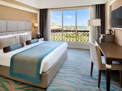 Helles Hotelzimmer mit großem Bett, Schreibtisch, Fenster mit Stadtblick und moderner Einrichtung.