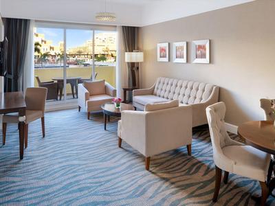 Helles Wohnzimmer mit hellblauem Teppich, grauem Sofa, Sesseln und drei Bildern an der Wand.