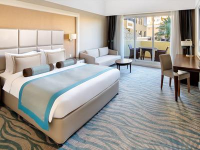Geräumiges Hotelzimmer mit großem Bett, Sofa, Schreibtisch und Balkon mit Blick ins Grüne.