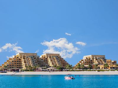 Dreieckige, terrassenförmige Gebäude am Strand mit blauem Himmel und türkisfarbenem Meer.