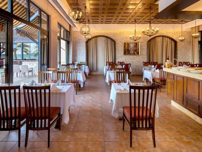 Elegantes Restaurant mit Holzmöbeln, weißen Tischdecken und großen Fenstern zur Terrasse.