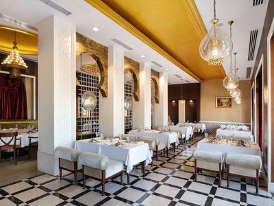Elegantes Restaurant mit weißen Tischdecken, goldener Decke und schwarz-weißem Fliesenboden.